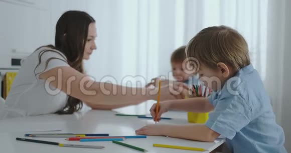 两个男孩的孩子和他的母亲坐在厨房里画画家庭幸福兄弟们在桌子旁画画实际视频的预览图