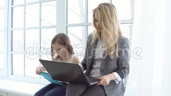 商业母亲带着笔记本电脑女儿坐在窗边视频的预览图