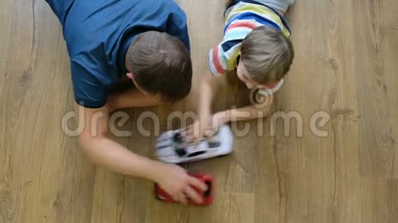 家庭观念男孩和爸爸在木地板上玩汽车有儿子的父亲直接上图视频的预览图