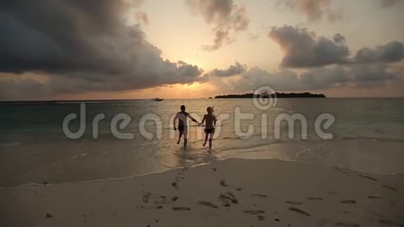 一对年轻幸福的夫妇在海洋中缓慢地牵着手奔向日落两个情人度蜜月视频的预览图