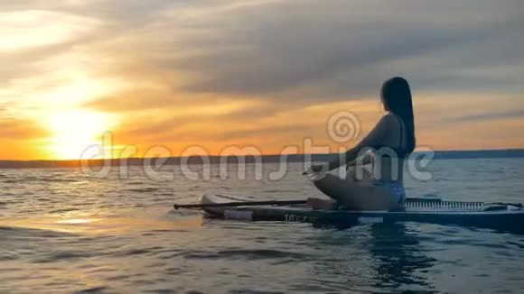 女孩在日落的背景下沉思女运动员在开阔的海洋里靠在冲浪板上休息视频的预览图