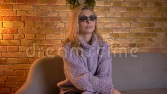 成年白种人金发女性坐在沙发上用3D眼镜在电视上看3D电影的特写镜头视频的预览图