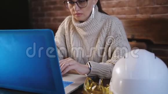 中年智能女工程师手打字在笔记本电脑键盘附近头盔和蓝图在现代玻璃桌上视频的预览图