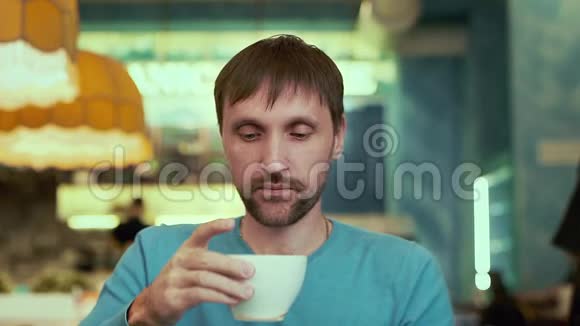 一个男人在咖啡馆里近距离喝着咖啡看着摄像机视频的预览图