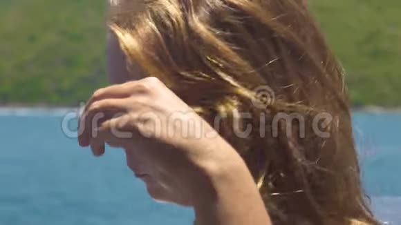 肖像年轻女子触摸金发在海洋和青山景观一头棕色金色头发的美丽女人视频的预览图