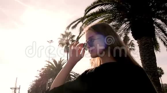 时尚少年戴着太阳镜站在海滩上手捧棕榈树戴墨镜的金发模特视频的预览图