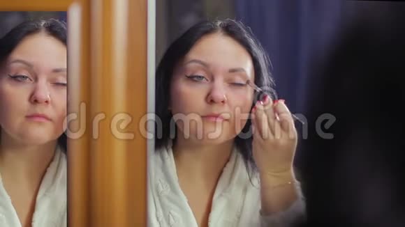 一个穿着白大褂的年轻女子在镜子前用刷子把化妆品的阴影涂在眼睑上视频的预览图