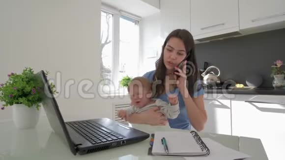 家庭压力多任务妈妈和哭泣的小男孩一起工作用手提电脑和手机聊天视频的预览图