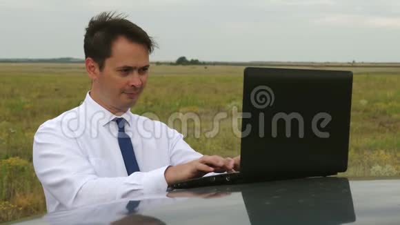 快乐的商人穿着蓝白衬衫在汽车车顶上的电脑上工作视频的预览图