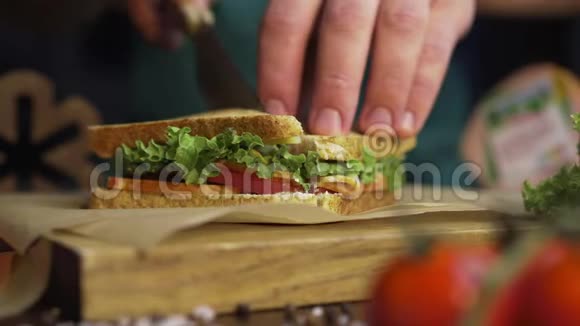 男人用锋利的刀在厨房的木板上把俱乐部三明治切成两半在家里做快餐厨师视频的预览图
