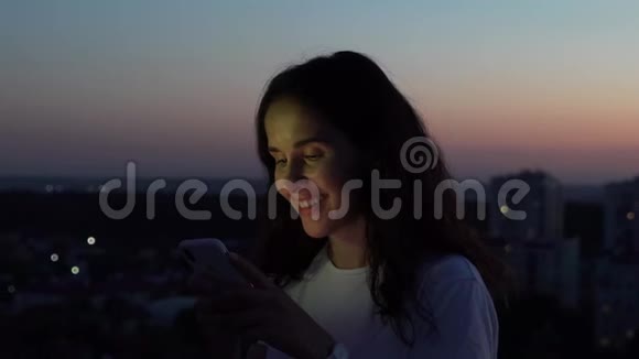 日落时分女孩在屋顶上的智能手机上打字视频的预览图