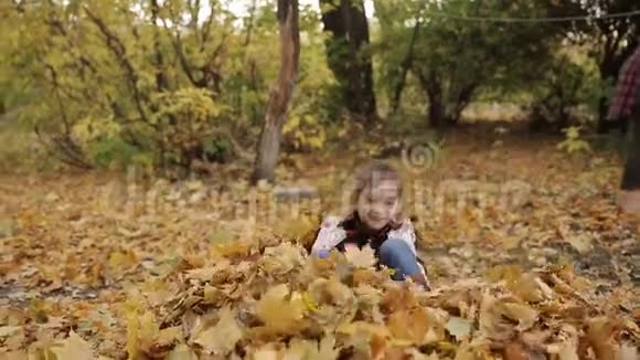 这个淘气的小女孩在一大堆黄色的叶子里快乐地玩耍女孩把黄叶扔上去视频的预览图