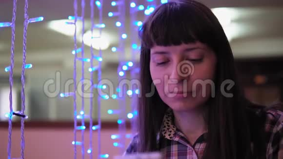 一个年轻的女人在蓝色的电动花环附近使用电话视频的预览图