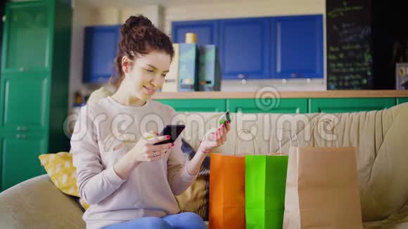 女人坐在沙发上提着购物袋用信用卡手机和移动应用程序在网上购物视频的预览图