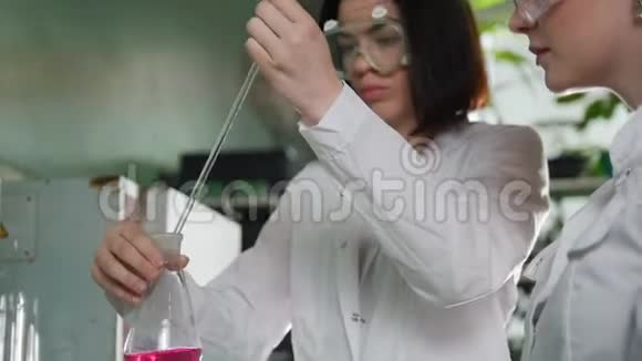 化学实验室两个年轻的女人在做实验烧瓶里的红色液体女人看着它视频的预览图