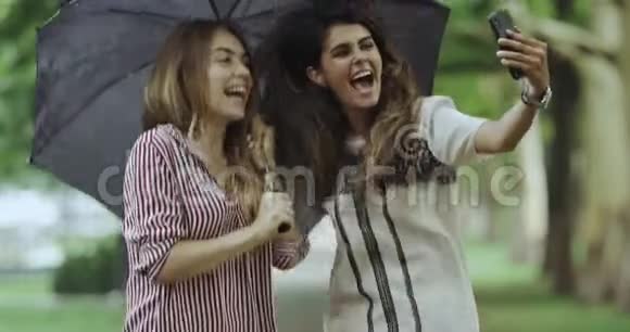 两个快乐的女孩同时跳着自拍在雨天的伞下视频的预览图
