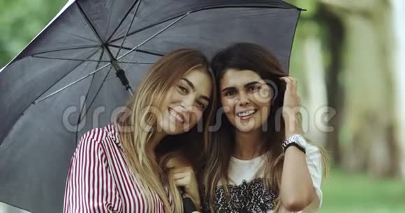 搞笑情绪的两个年轻女性伞下直视镜头大笑起来视频的预览图