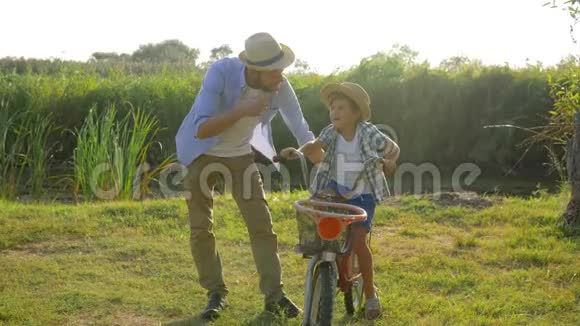 爸爸在日落和户外自然的背景下教儿子如何在乡下骑自行车视频的预览图