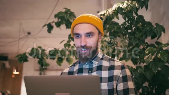 戴着黄色帽子的嬉皮士在笔记本电脑上用视频聊天与朋友或商业伙伴交流视频的预览图