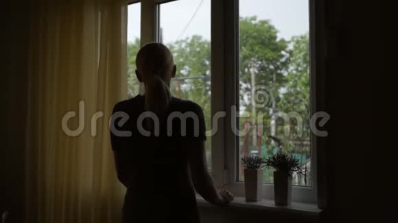 一个中年妇女站在窗前若有所思地透过玻璃看着雨视频的预览图