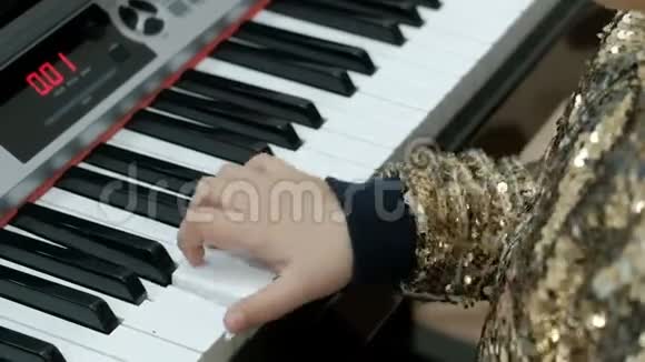 穿着闪亮的金色衬衫的少女弹电钢琴孩子们手指按合成器的键视频的预览图