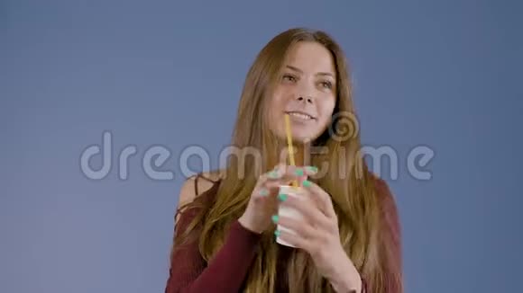 一个年轻的女孩拿着一个纸杯喝酒在蓝底的工作室里广告摄影视频的预览图