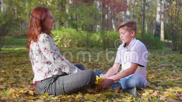 妈妈和儿子在秋天公园玩他们扔黄叶快乐的户外消遣视频的预览图