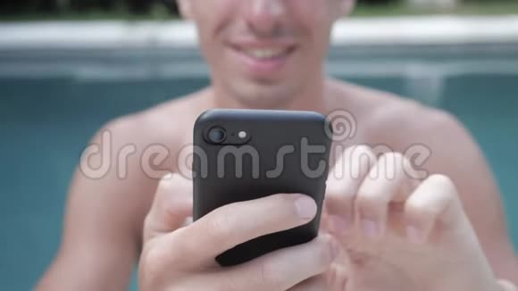 迷人英俊的年轻人长得漂亮在社交媒体上滚动着智能手机在游泳池里休息视频的预览图