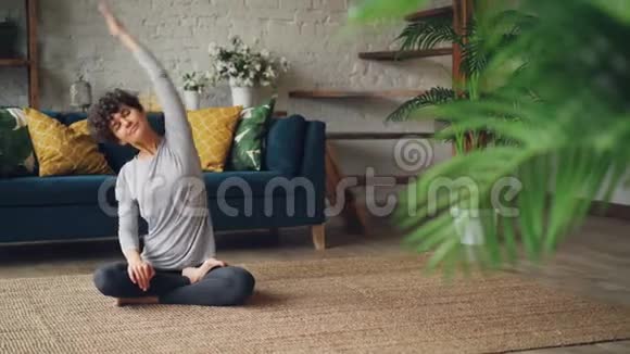 以健康为导向的年轻女性伸展手臂和身体然后以莲花的姿势休息双手跪坐视频的预览图