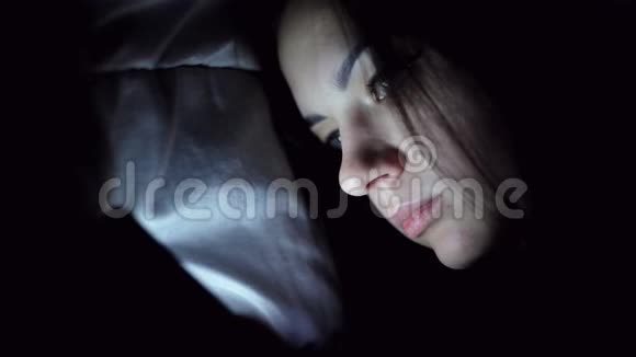 躺在毯子下用手机在床上打字的年轻女子视频的预览图