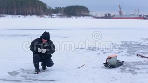 穿着深色冬装的渔夫们用鱼饵准备钓钩并准备在冰冻的河流上进行冬季冰钓视频的预览图