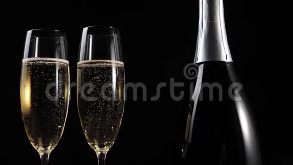 好香槟酒两个带香槟的玻璃杯和一个带香槟的瓶子放在黑色背景的木桌上长笛视频的预览图