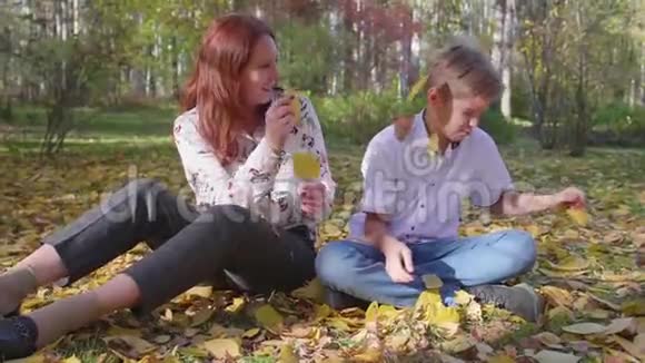 妈妈和儿子在秋天公园玩他们扔黄叶快乐的户外消遣视频的预览图