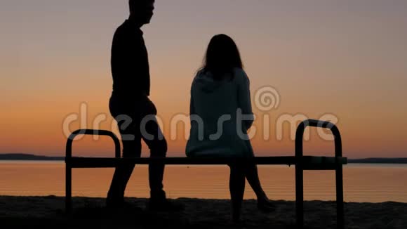 爱的情侣坐在沙滩上的长凳上享受日落视频的预览图
