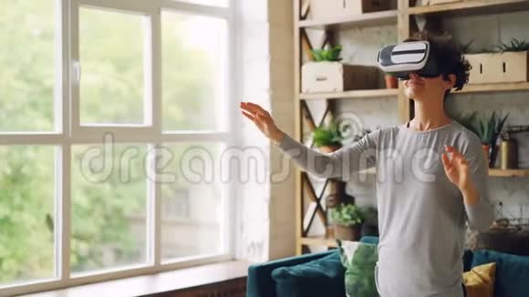 幸福的年轻女士戴着人造现实眼镜站在阁楼风格的公寓里做手势曲线视频的预览图