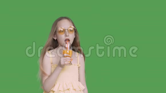 年轻的女孩在绿色背景下用吸管从玻璃中喝橙汁少女喝水果鸡尾酒视频的预览图