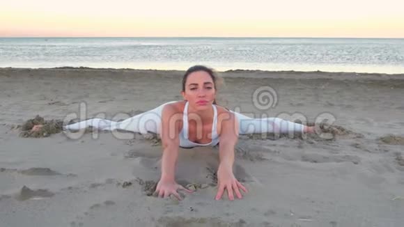 日出时年轻女子坐在沙滩上做瑜伽伸展运动视频的预览图
