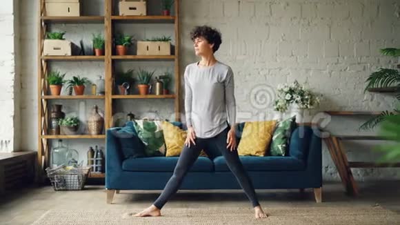 漂亮的女孩正在家里做瑜伽练习伸展身体站在家里的地板上集中练习青年视频的预览图