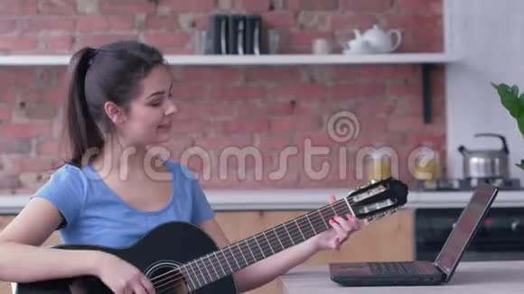 令人惊叹的音乐家女性学习弹吉他使用笔记本电脑在线视频教学享受音乐视频的预览图