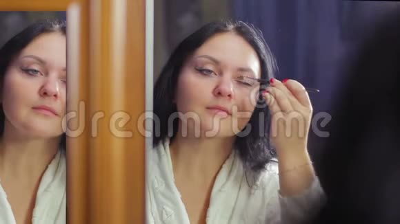 一个穿着白大褂的年轻女人在镜子前用化妆刷做眼妆视频的预览图