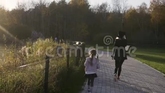 日落时母亲和女儿在公园里散步光线泄漏秋天的天气在夏季公园的孩子和家长视频的预览图