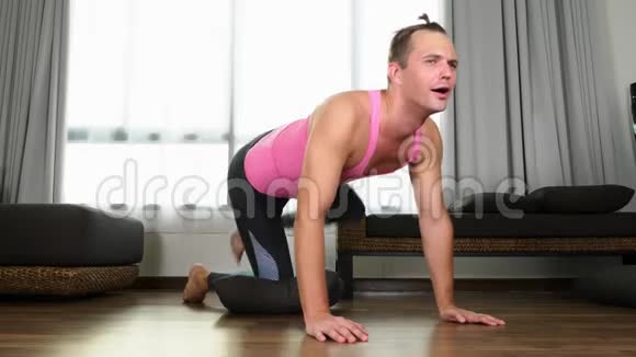 贪玩的帅哥穿着一件粉红色的t恤从事健身在他家的客厅里视频的预览图