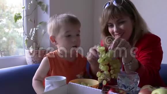 一个非常可爱的小孩子和一个有魅力的女人吃葡萄他们在房间里健康食品概念视频的预览图