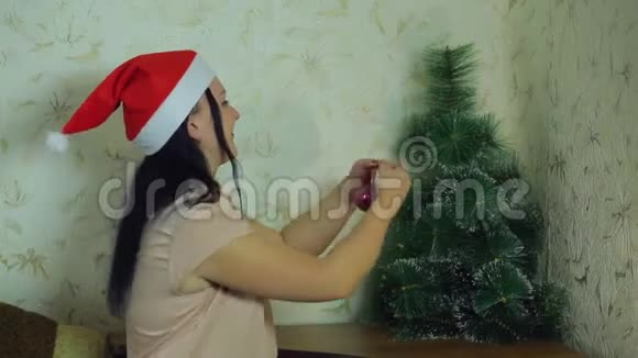 一个戴圣诞老人帽子的年轻女子在家里装饰圣诞树视频的预览图