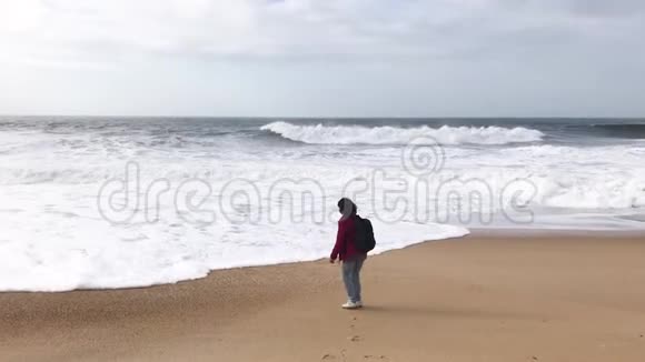 一个年轻的女人背着背包在海边玩海浪视频的预览图