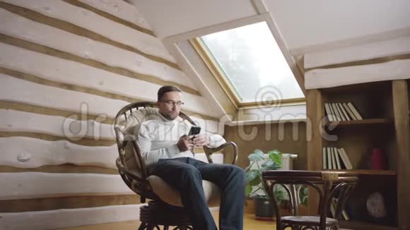 戴眼镜的漂亮男人带着手机坐在阁楼上视频的预览图