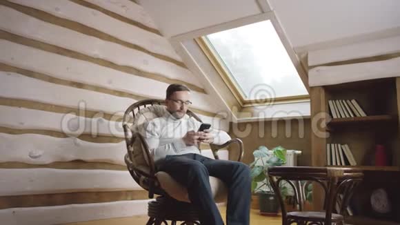 戴眼镜的胡子男在阁楼上的智能手机上发短信视频的预览图