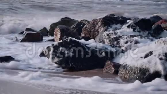 海浪拍打着大海中的一簇黑色石头拍打着天空的沙滩视频的预览图