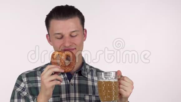 年轻迷人的男人开心地笑着喝着美味的啤酒拿着椒盐卷饼视频的预览图
