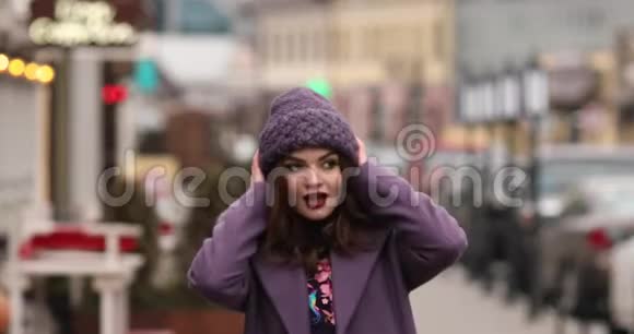 穿着紫色冬帽和外套的迷人女孩用鲜艳的化妆在街上行走视频的预览图
